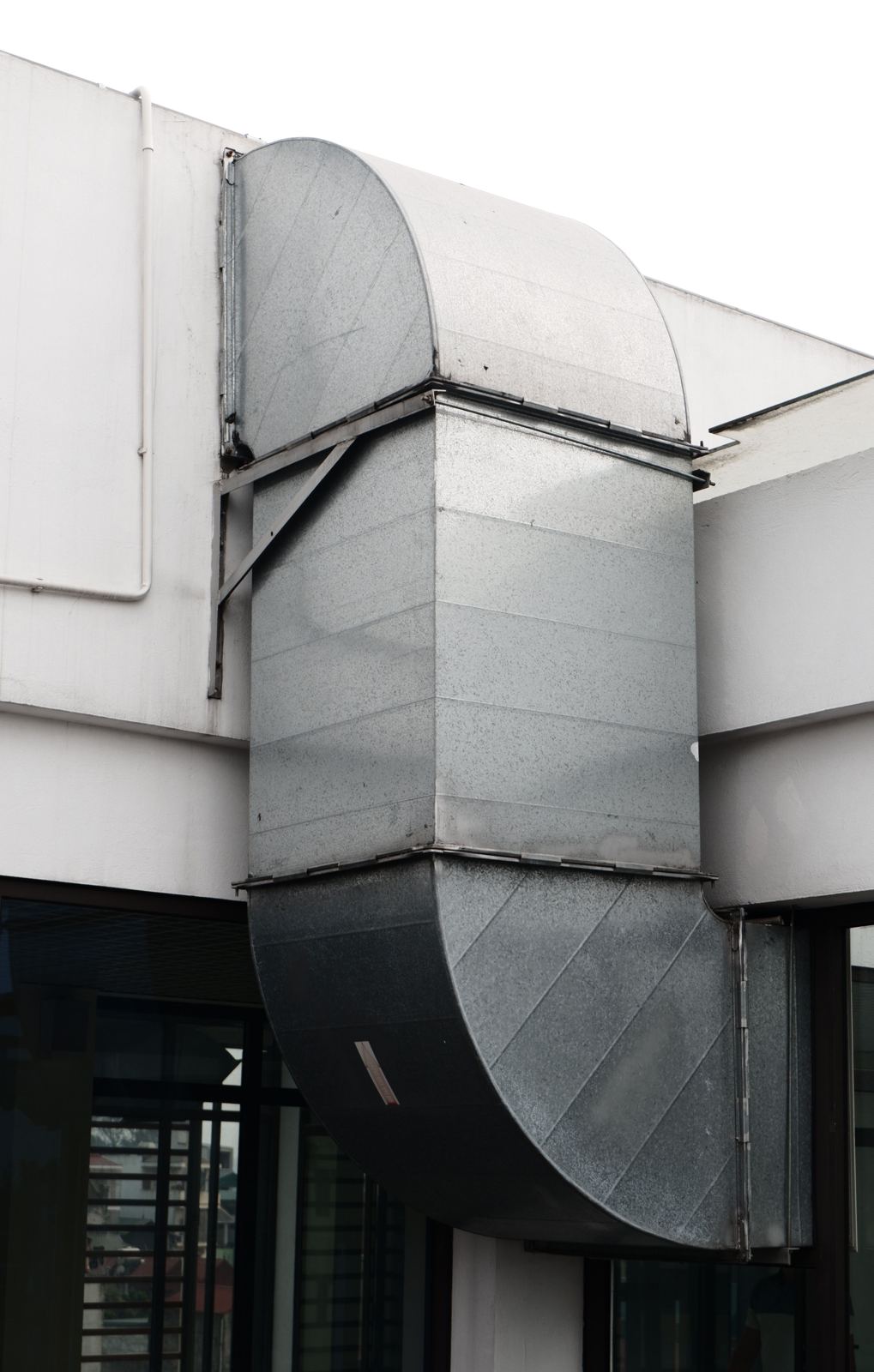 Large galvanized supply duct with curved elbows mounted outside a commercial building
