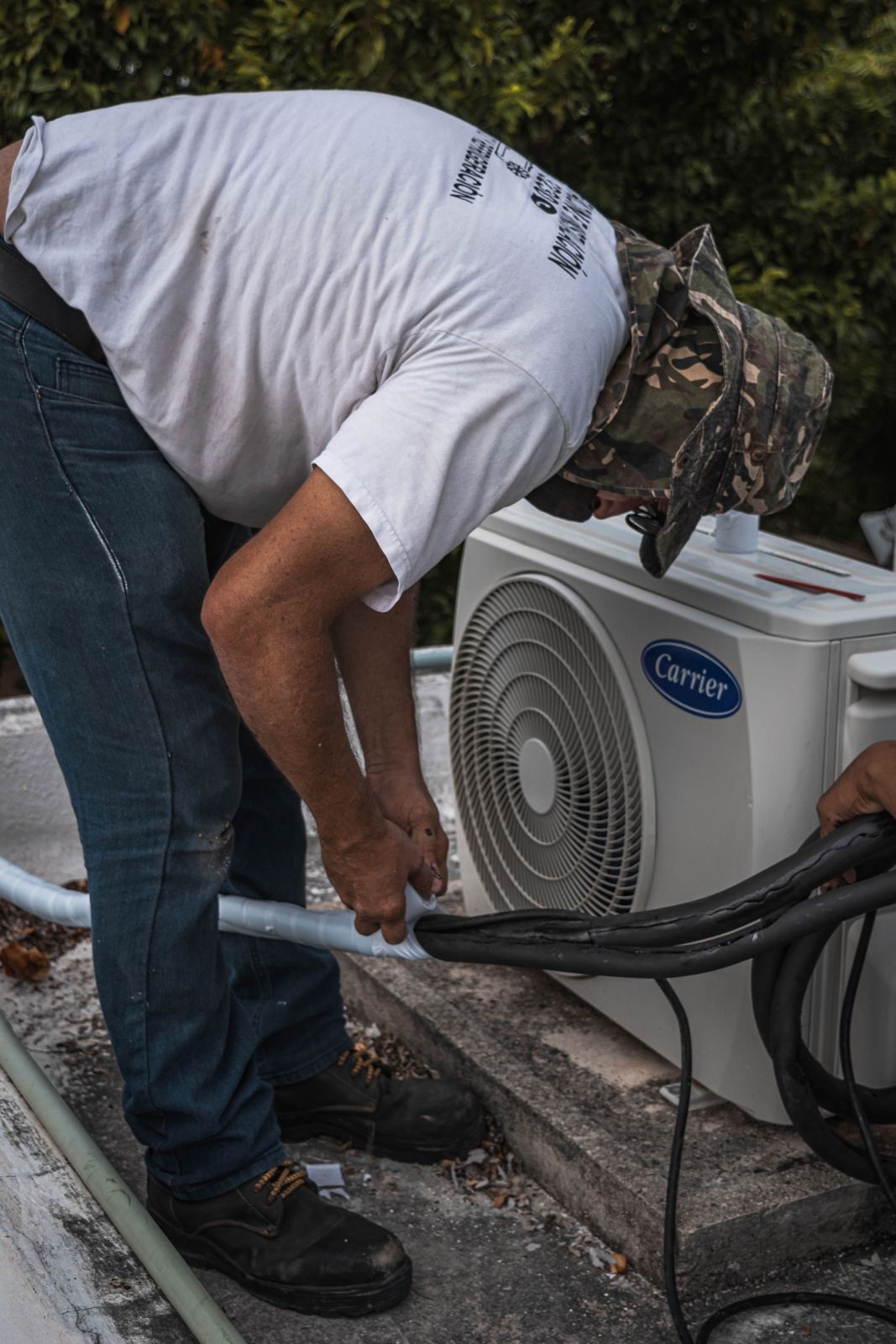 HVAC installer wrapping the insulated refrigerant line set beside a new outdoor condenser