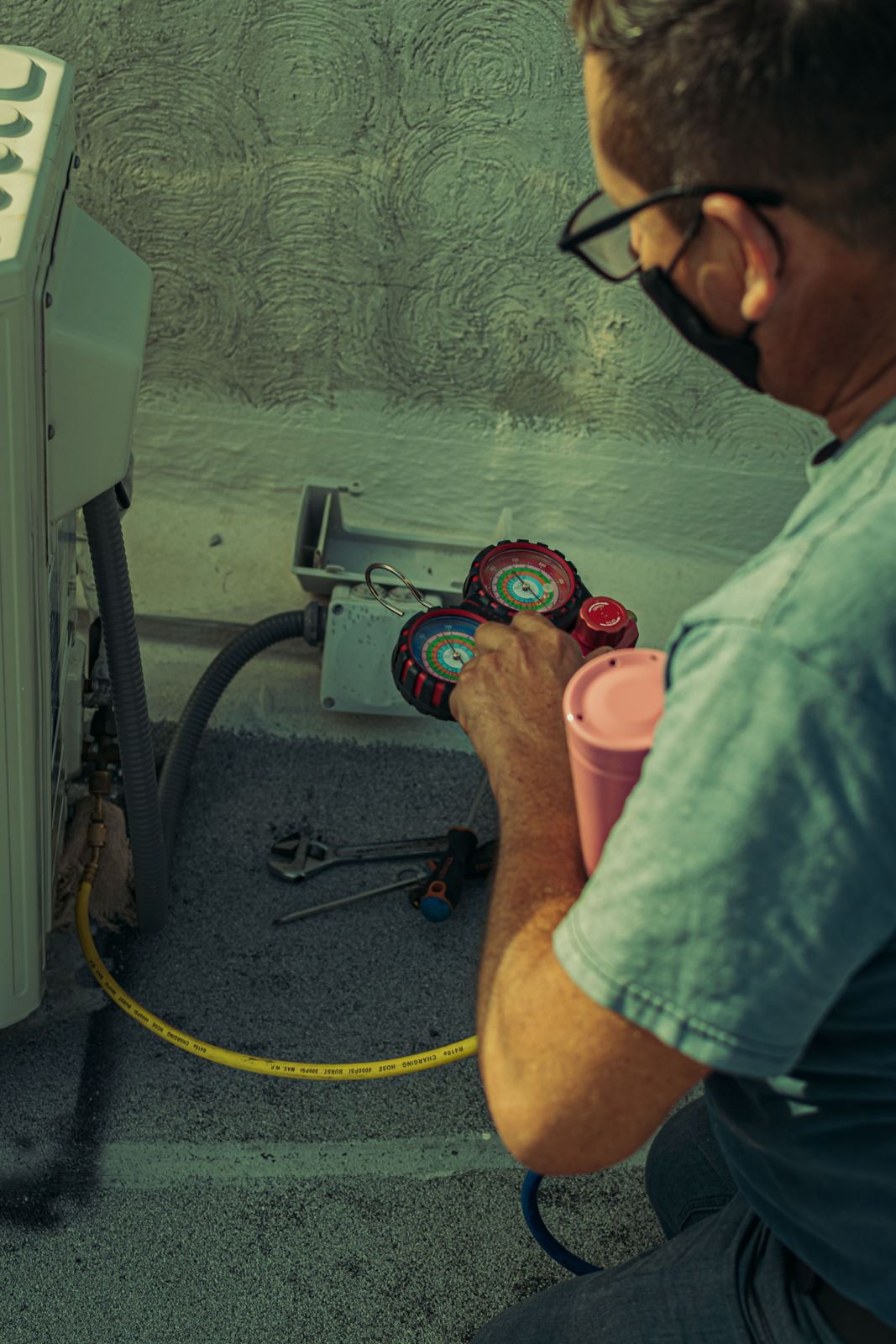 Technician reading manifold gauges connected to an outdoor air conditioning unit