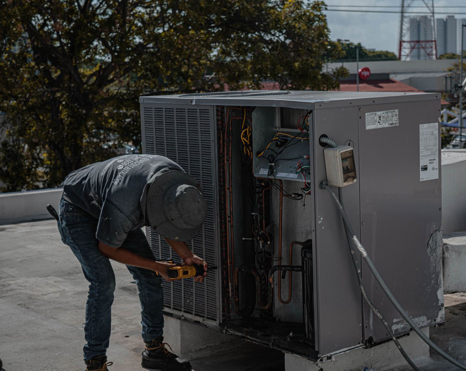 Technician working on an open rooftop packaged HVAC unit with a cordless drill