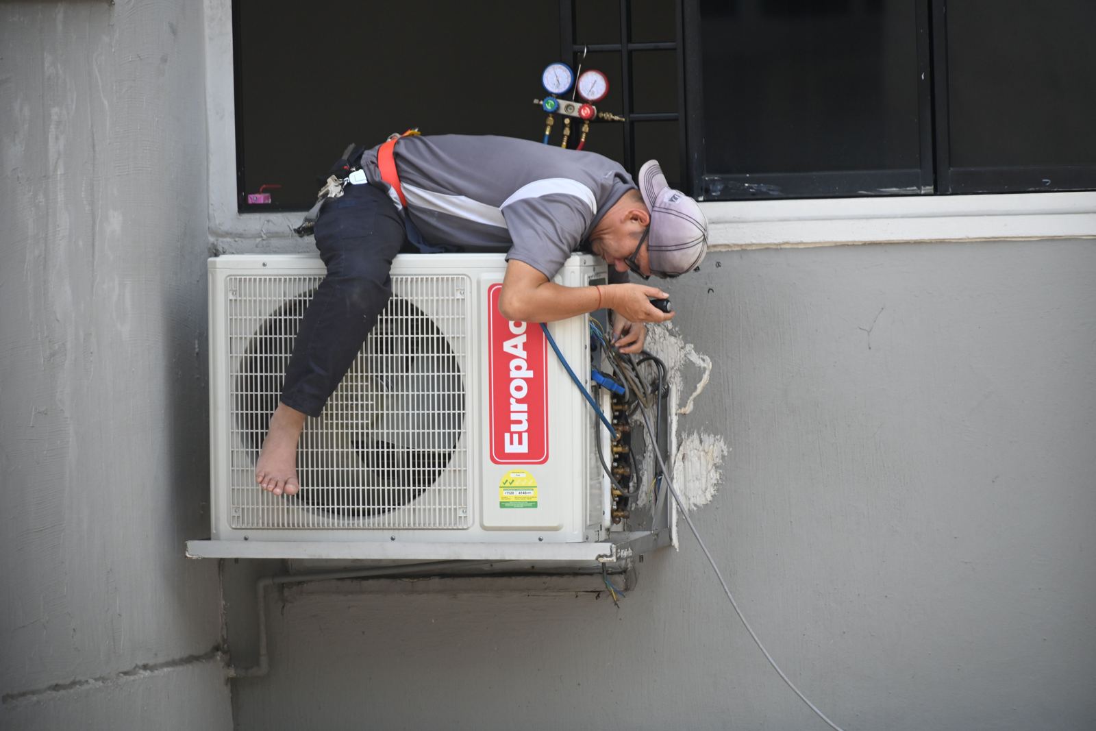 Installer working on the connections of a wall-mounted split system outdoor unit on a building exterior